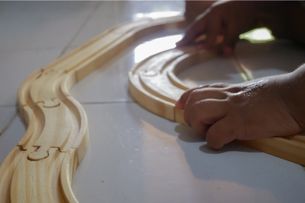 A child's hands closing the last curve of a birch ball track on the living room floor.