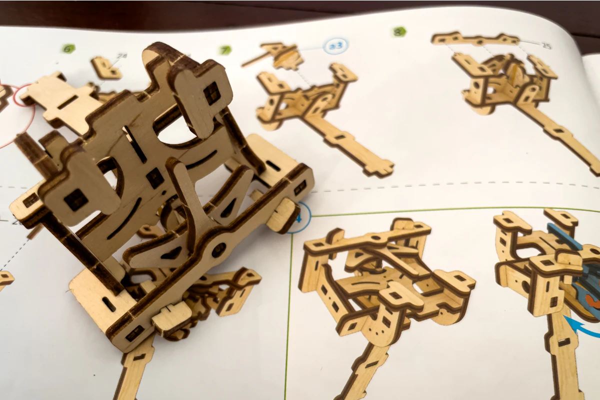 Punched birch sheets beside a half-assembled maze frame, parts still numbered in their sprues.